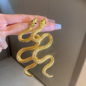 Exaggerated golden snake earrings with green gemstone eyes and metallic scale texture