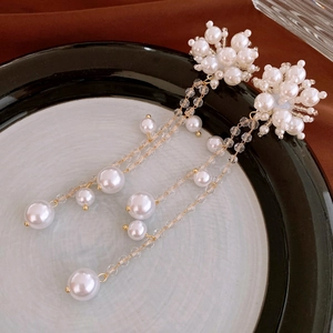 Detail of elegant pearl flower earrings with long gold tassels on a ceramic plate