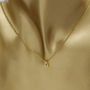 Close-up of golden letter A pendant necklace on mannequin showing polished finish
