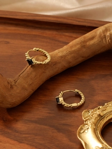 Close-up of gold twist hoop earrings with black square zircons on rustic wood and silk
