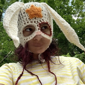 Macro detail of handmade crochet rabbit hat featuring orange star and brown knit ties
