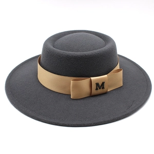 Makroaufnahme eines dunkelgrauen Wollhutes mit Seidenband und goldenem M-Buchstaben