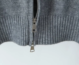 Detailed close-up of the metal two-way zipper on this grey knit cardigan sweater