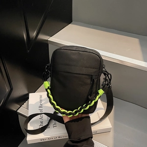 Detail of small black crossbody bag with vibrant neon green woven handle and zipper pockets