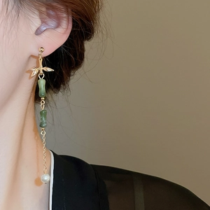 Detailed close-up of bamboo tassel earrings with gold leaf finish and pearl drop