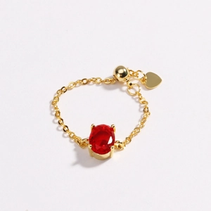 Detail of gold chain ring with oval red zircon, adjustable slider, and heart charm