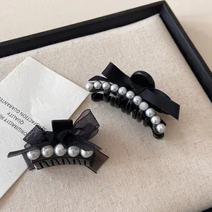 Detail of elegant black ribbon hair clips with embedded white pearls on fabric background