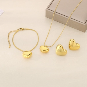 Detailed set of polished gold heart necklace, bracelet and earrings on beige texture
