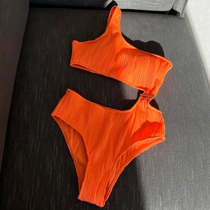 Close-up of orange one-shoulder ribbed swimsuit featuring stylish side cutout and metal ring