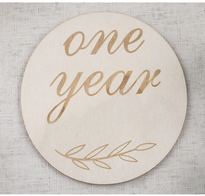 Gros plan d'un disque de jalon en bois avec gravure cursive one year et motif de feuille
