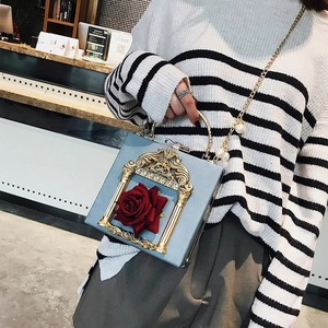 Detail of light blue box bag featuring a 3D red rose and golden embossed frame with pearls
