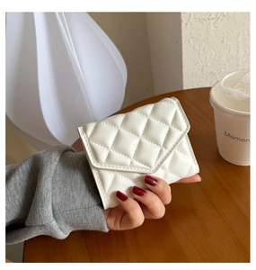 Close-up of white quilted PU leather tri-fold wallet held against a wooden desk background
