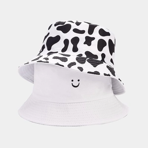 Detail of reversible bucket hats featuring cow print and white smiley face embroidery