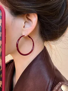 Close-up of oversized wine red hoop earrings with glossy finish on model with leather jacket