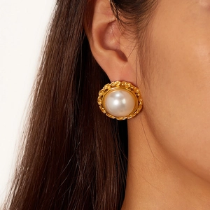 Close-up of vintage pearl earrings with gold-plated textured frame on ear
