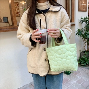 Close-up of mint green quilted tote bag with floral patterns held in hand outdoors