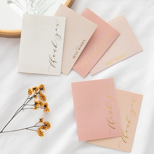 Minimalist gold foil thank you cards in assorted pink and beige tones on white fabric