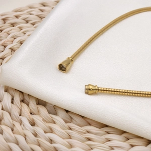 Detail of gold snake chain necklace with magnetic cylindrical clasp on white silk