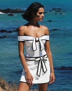 Detail of off-shoulder white swimsuit with black contrast bows in a beach setting