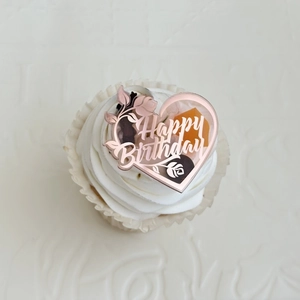 Detailed close-up of rose gold acrylic heart cake topper with floral engraving and Happy Birthday
