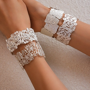 Detail of four matte silver wide cuff bracelets with floral cutout and hammered texture