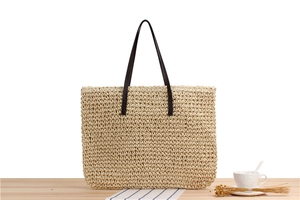 Detail of hand-woven straw tote bag with brown leather handles on wooden surface