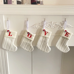 Close-up of white knitted Christmas stockings with embroidered red LOVE letters and mini hats