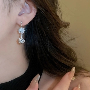 Macro shot of silver crystal flower earrings worn by a model with dark wavy hair