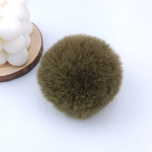 Close-up of deep olive green 8cm faux rabbit fur pom-pom on a minimalist white surface