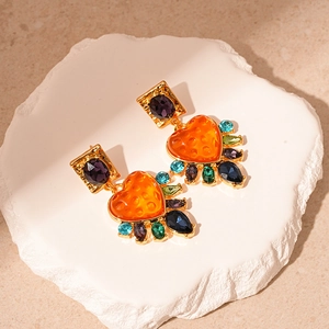 Vintage gold heart earrings with colorful resin gems on a white plaster tray