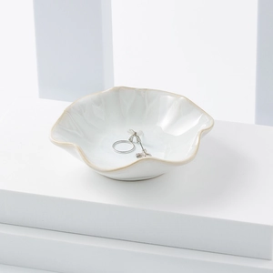 Macro shot of wavy edge ceramic jewelry tray with earrings and ring on white base