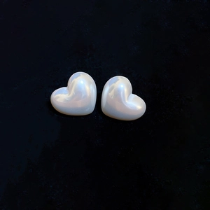 Detailed view of pearlescent white heart-shaped earrings on a dark textured background