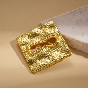 Detail of golden square brooch with hammered texture and keyhole cutout on leather surface