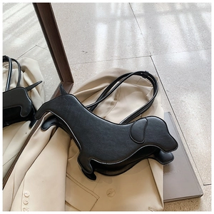 Detail shot of black dachshund shaped shoulder bag on beige blazer with leather texture