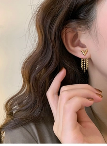Close-up of gold V-shaped stud earrings with hanging beaded tassel chains on model