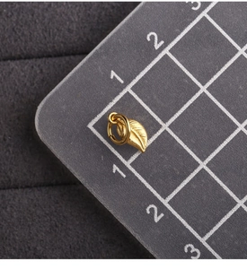 Macro shot of gold leaf pendant on a grey scale mat showing exact size measurements