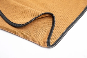Close-up of camel twill weave fabric with black leather edge and neat stitching detail