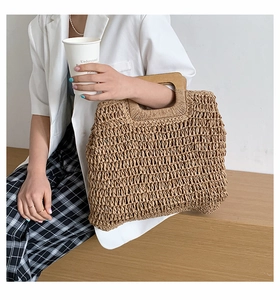 Detail of a natural straw woven handbag with smooth wooden handles held by a woman