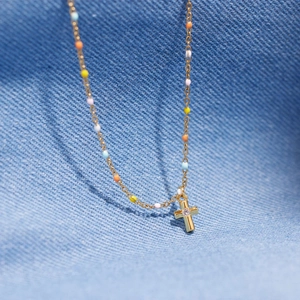 Gold s925 silver necklace with cross pendant and colorful beads on blue denim
