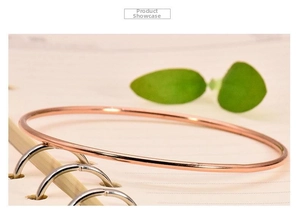 Polished 18K rose gold plated 2mm minimalist stainless steel bangle on an office desk