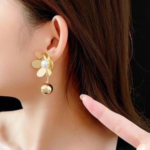 Gros plan de boucles d'oreilles fleur dorées avec perle et sphère portées par un mannequin
