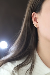 Close-up of golden honeycomb stud earrings with micro diamond inlay on a female model