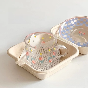 Detail of glass cup with tulip pattern and blue checkerboard coaster on beige display stand