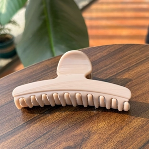 Macro detail of nude pink hair claw clip with marble texture on dark wood surface
