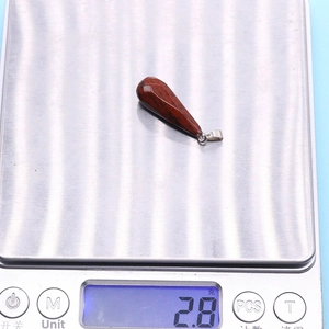 Teardrop gemstone pendant in reddish brown shown on a scale weighing 2.8 grams