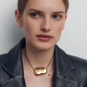 Close-up of golden irregular geometric pendant on black cord worn by a female model