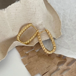 Macro view of gold twisted rope texture on a U-shaped earring with a natural paper backdrop