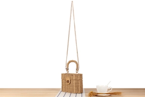 Detail of woven straw box bag featuring leather clasp and golden metal chain strap
