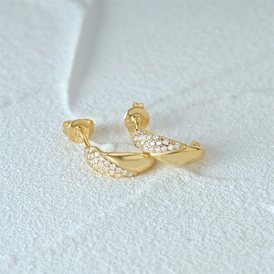 Detail of C-shaped gold earrings featuring paved white zircons and polished finish