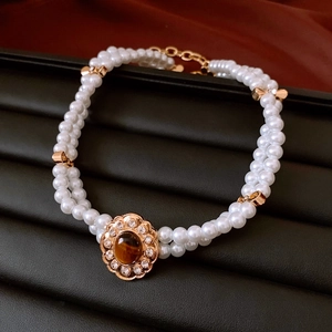 Dettaglio del ciondolo a fiore dorato con pietra marrone su collana di perle a due strati